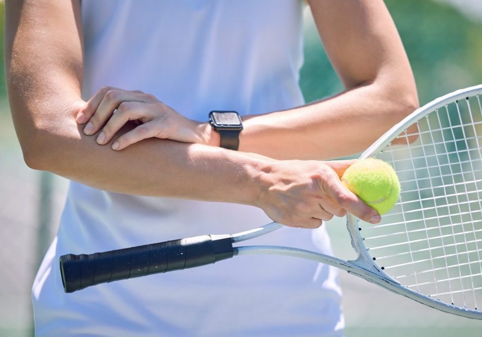 Sports, arm pain and tennis player with a racket and ball standing on a court during for a match. Closeup of a health, strong and professional athlete with equipment touching a medical elbow injury